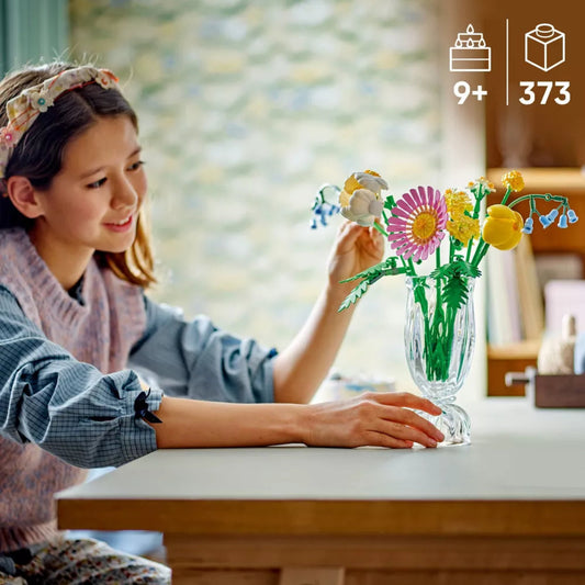 Girl arranging flowers in a glass vase with LEGO flowers, sitting at a table.