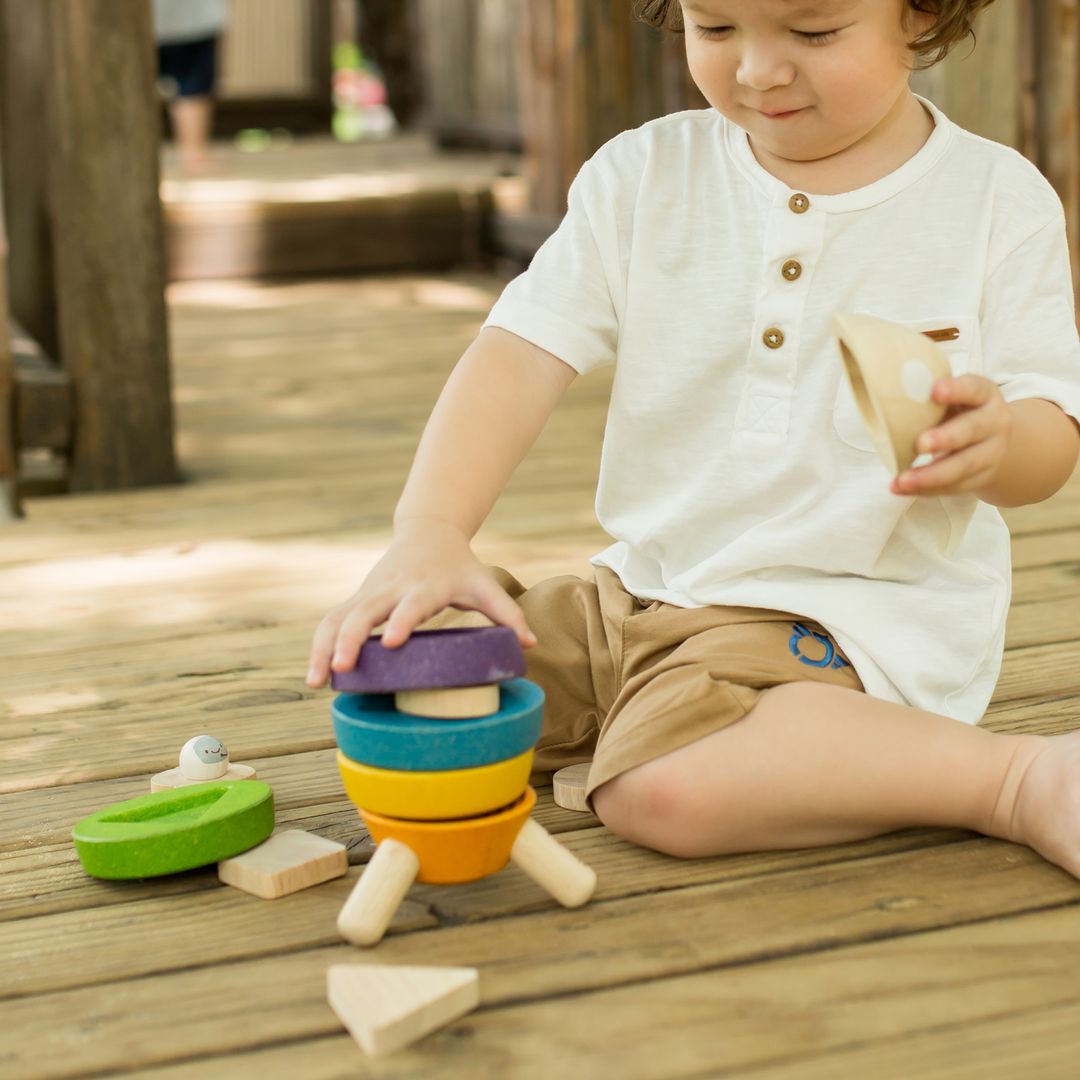A young child placing the wooden nose cone onto the fully stacked PlanToys eco-friendly rocket toy.