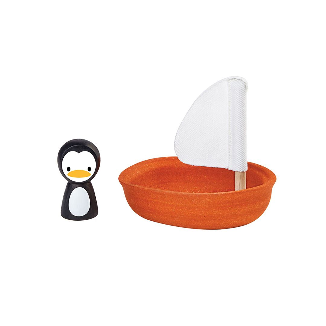 Angled view of the non-toxic PlanToys orange sailing boat and cute penguin companion ready for water play.