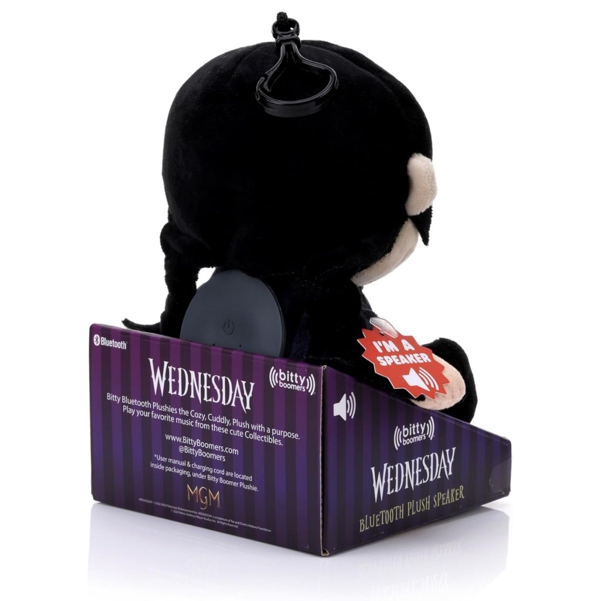 Back view of the Wednesday Addams plush speaker inside its packaging, showing the top carrying clip and the purple display box.