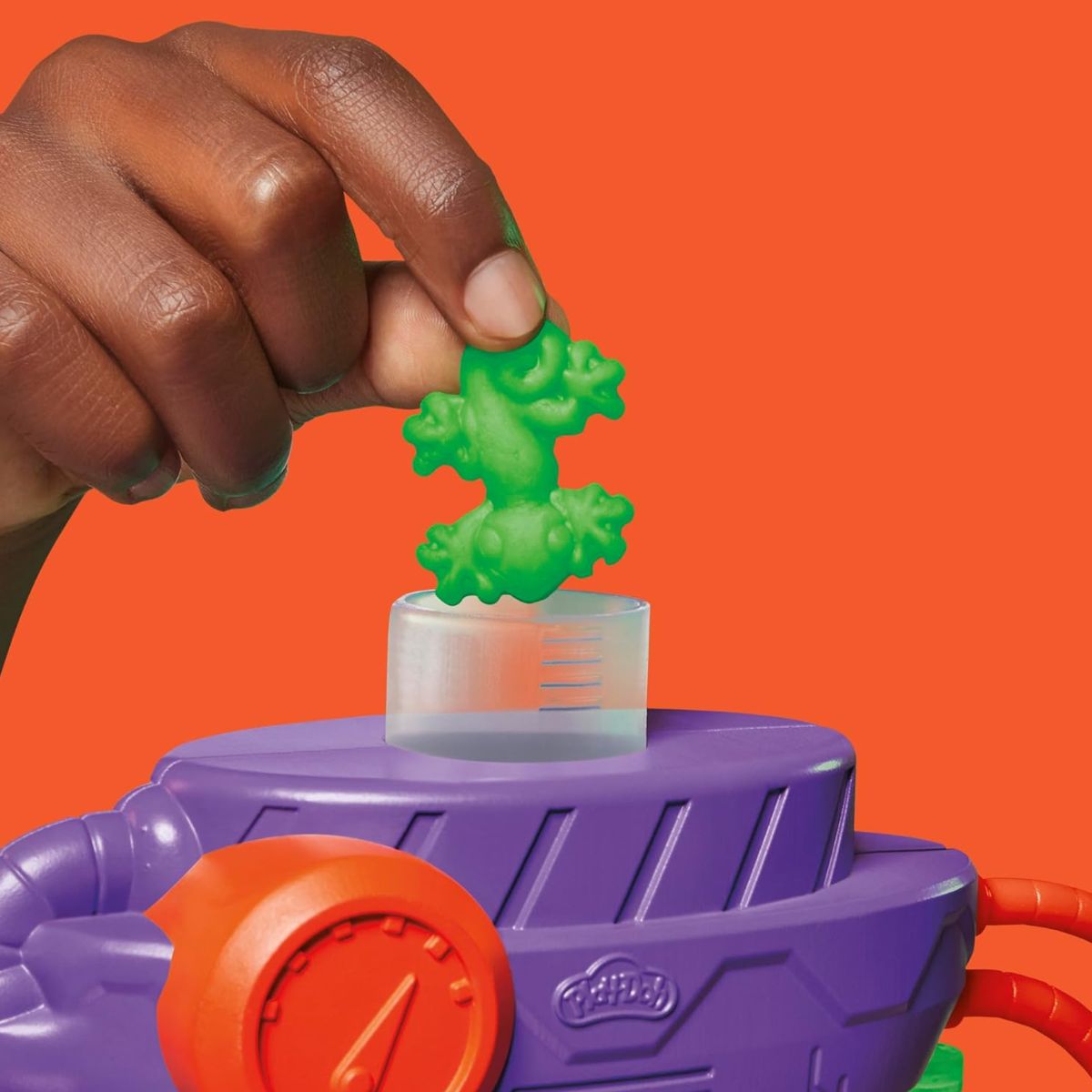Detail thumbnail showing hands inserting green Play-Doh compound into the top opening of the mutation chamber.
