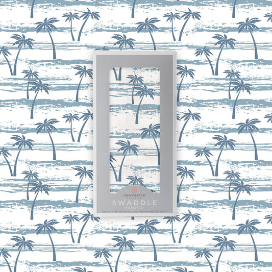 Flat lay of the Newcastle Classics Ocean Palm Trees bamboo muslin swaddle blanket shown with its branded grey packaging box in the center against a matching palm tree pattern background.