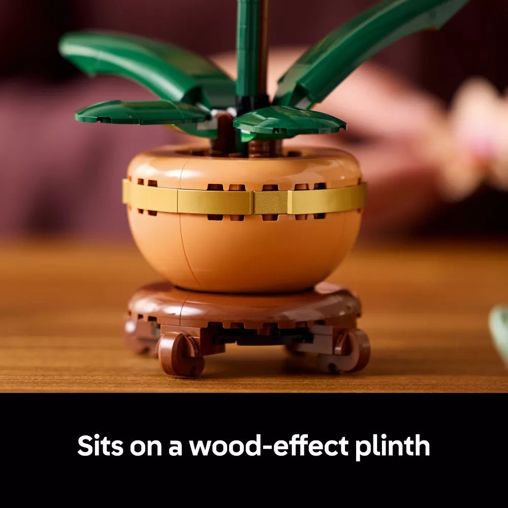 Small decorative plant made of interlocking bricks on a wood-effect plinth with blurred background