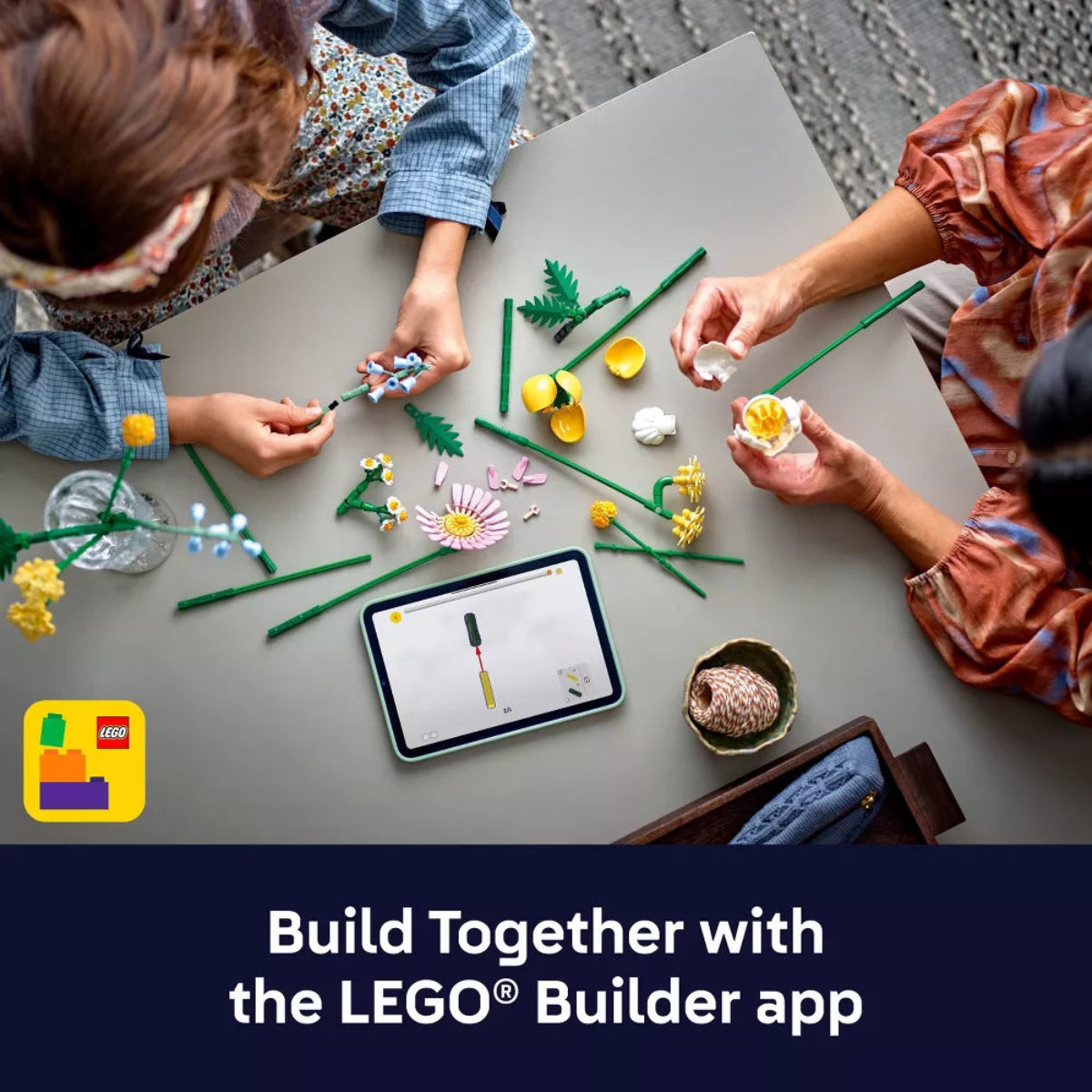 Two people building with LEGO pieces on a table, using the LEGO Builder app.
