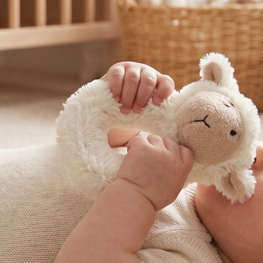 A close-up view of a baby's tiny hands gripping and playing with the Happy Horse Lammy Lamb cream plush rattle.