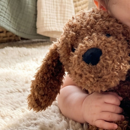A close-up view of a baby cuddling the soft Happy Horse Labradoodle Larry brown curly puppy plush closely against their cheek.
