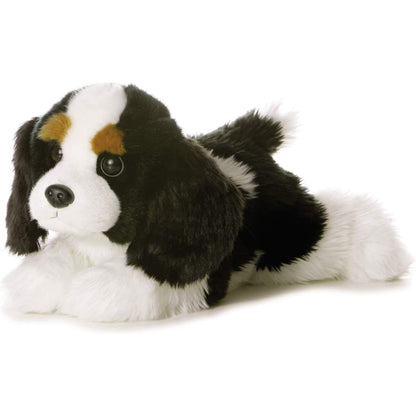 Angled front view of the Aurora Flopsie Charles the Cavalier King Charles Spaniel 12-inch plush resting on its belly, featuring a black, white, and tan tri-color coat.