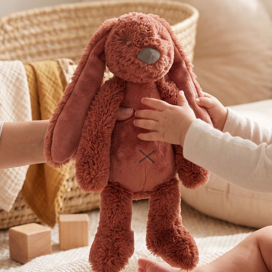 A young child's hands interacting with the Happy Horse Rabbit Richie rusty orange plush toy in a cozy nursery setting near wooden blocks.