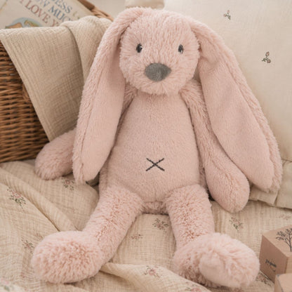 Happy Horse Rabbit Richie old pink plush toy sitting comfortably on a soft blanket inside a cozy nursery setting.