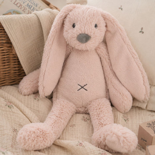 Happy Horse Rabbit Richie old pink plush toy sitting comfortably on a soft blanket inside a cozy nursery setting.