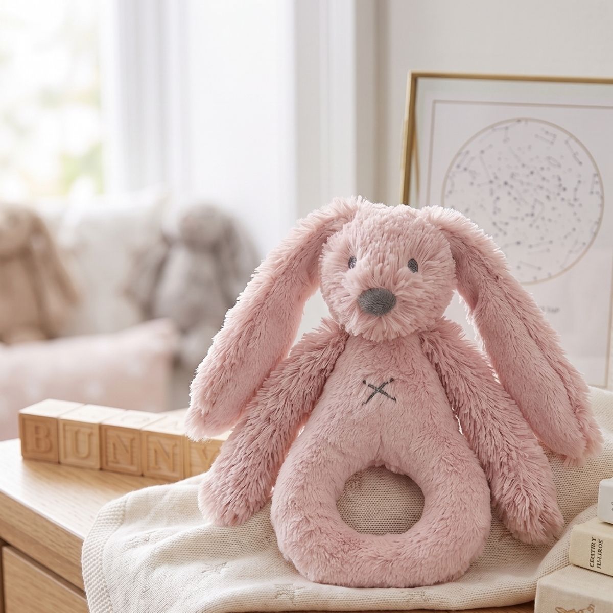 Happy Horse Rabbit Richie old pink plush rattle sitting upright on a soft blanket in a cozy, bright nursery setting.