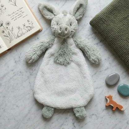 Happy Horse Donkey Diego plush lovey laid flat on a gray surface next to an open baby book and a green blanket.