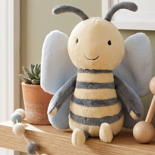 Happy Horse Bee Benja plush bee sitting on a wooden nursery shelf next to a small potted plant and a wooden bead garland.