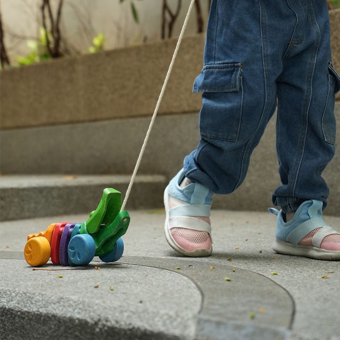 Close-up of a toddler's legs taking steps outdoors while pulling the durable PlanToys wooden alligator.