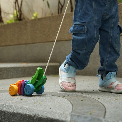 Close-up of a toddler's legs taking steps outdoors while pulling the durable PlanToys wooden alligator.