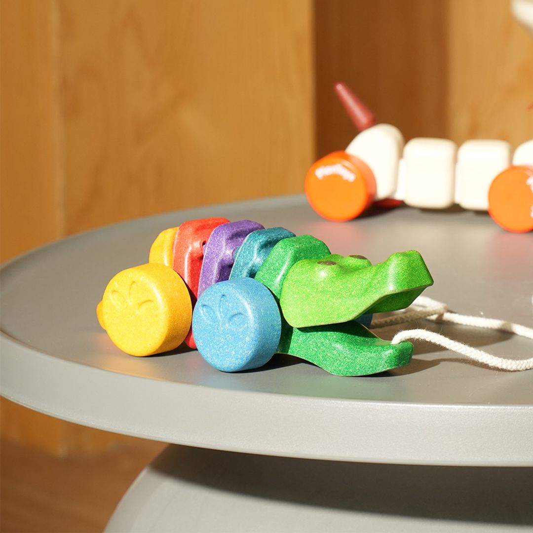 Detailed lifestyle shot of the heirloom-quality PlanToys wooden alligator resting on a round grey table.
