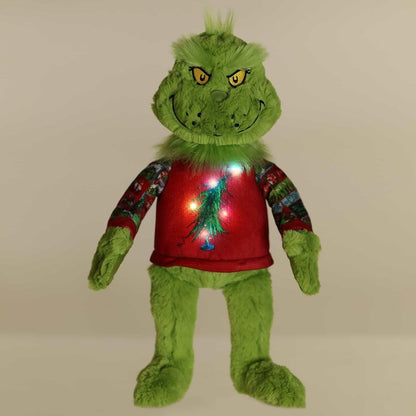 Darkened room view of the standing Grinch plush showcasing the colorful, glowing lights illuminating the Christmas tree on his ugly sweater.
