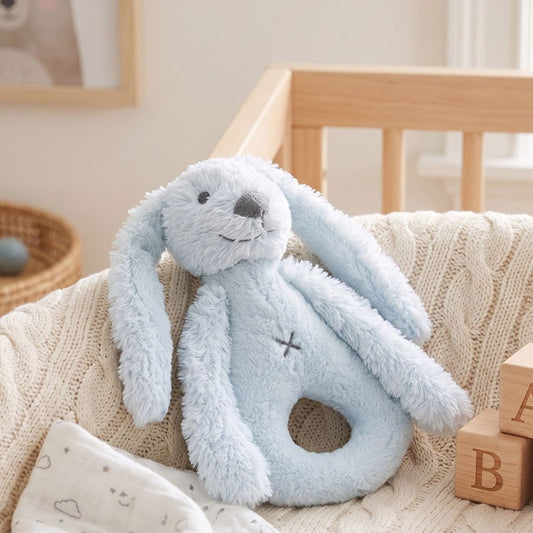 Happy Horse Rabbit Richie blue plush rattle resting on a soft blanket inside a woven nursery basket.