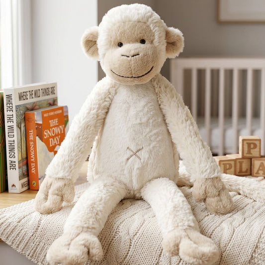 Happy Horse Monkey Mickey plush toy sitting on a textured cream blanket in a cozy nursery setting with books in the background.