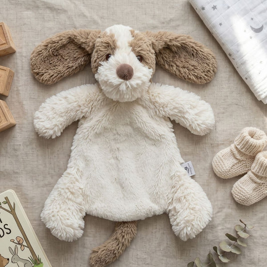Happy Horse Dog David plush lovey resting on a soft blanket next to wooden blocks and knit baby booties.