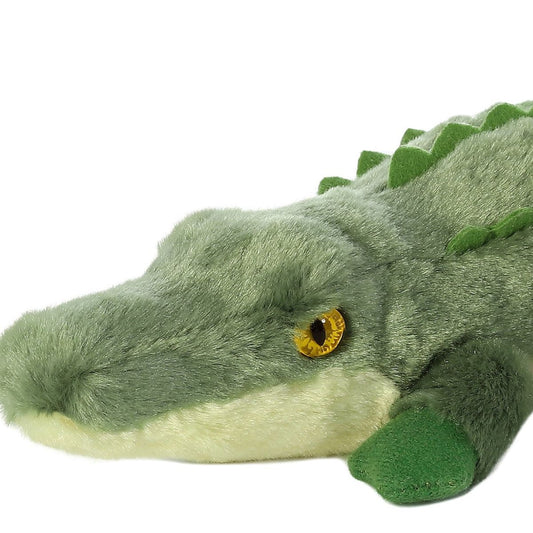 Close-up view of the adorable Aurora Swampy Crocodile stuffed animal featuring a long green snout, a striking yellow eye, and dark green front feet.