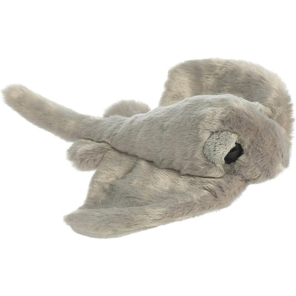 Angled front view of the Aurora Mini Flopsie Stingray 8-inch plush resting on its belly, featuring soft grey fur and prominent eyes.