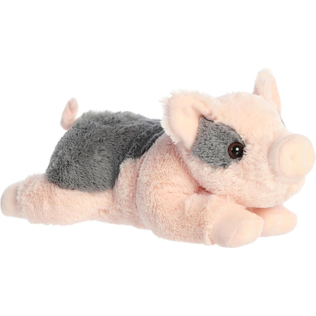Angled side view of the Aurora Flopsie Tidbit the Pig 12-inch plush resting on its belly, featuring soft pink fur with a dark grey patch on its back.