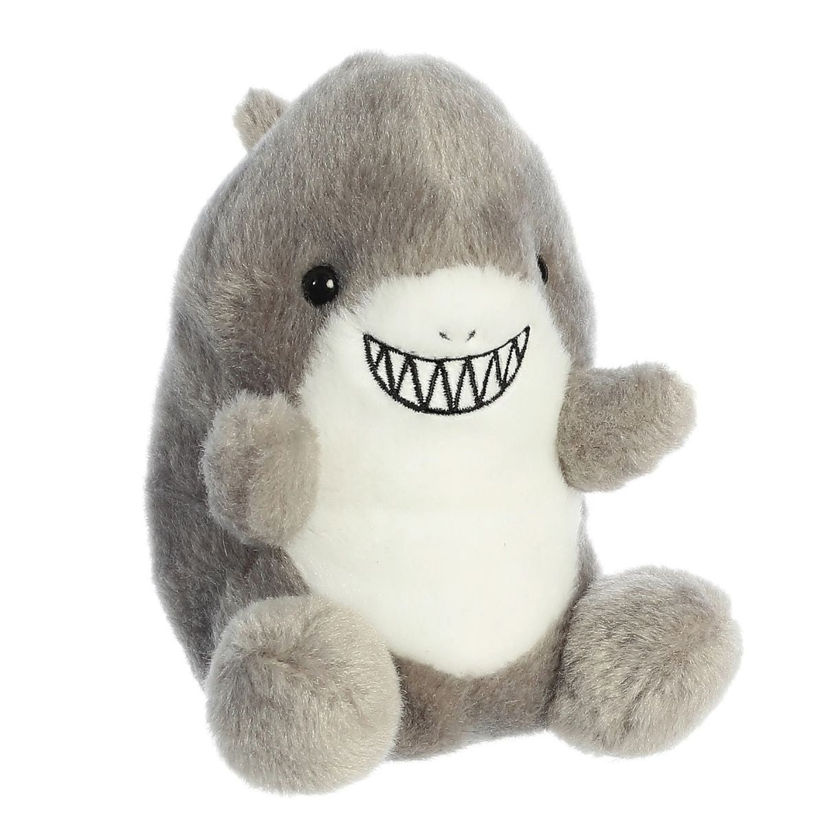 Angled view of the Aurora Palm Pals 5-inch Chomps Shark plush sitting upright, showing its soft grey back, white belly, and toothy grin.