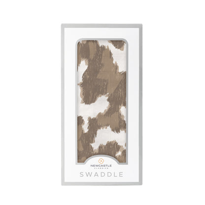 Straight front view of the packaged cowhide print baby swaddle blanket in a Newcastle Classics box.