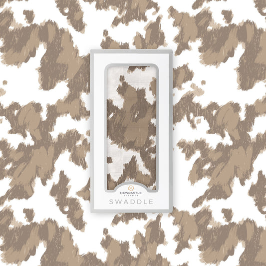 Flat lay of the Newcastle Classics Yellowstone Cowhide bamboo muslin swaddle blanket shown with its branded white packaging box in the center.