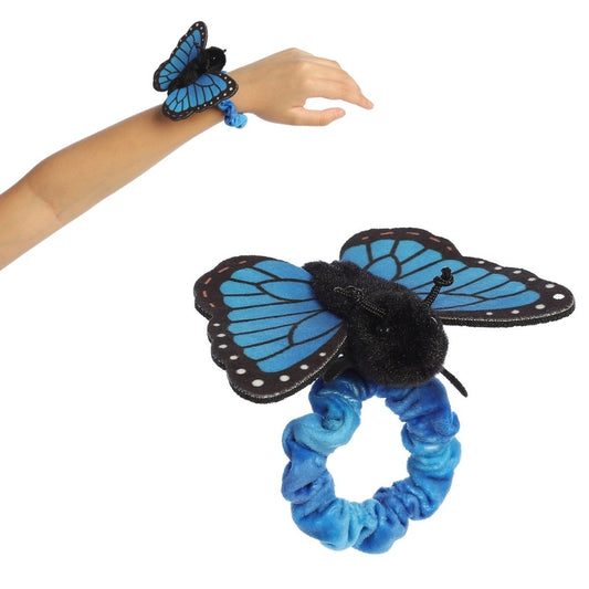 A person's arm wearing the 5-inch Aurora Wrist Flingers Blue Morpho Butterfly plush with a close-up of the bright blue butterfly on its wristband.