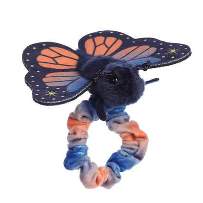 Side profile view of the wearable butterfly plush showing its fluffy dark body and outstretched sunset-colored fabric wings.