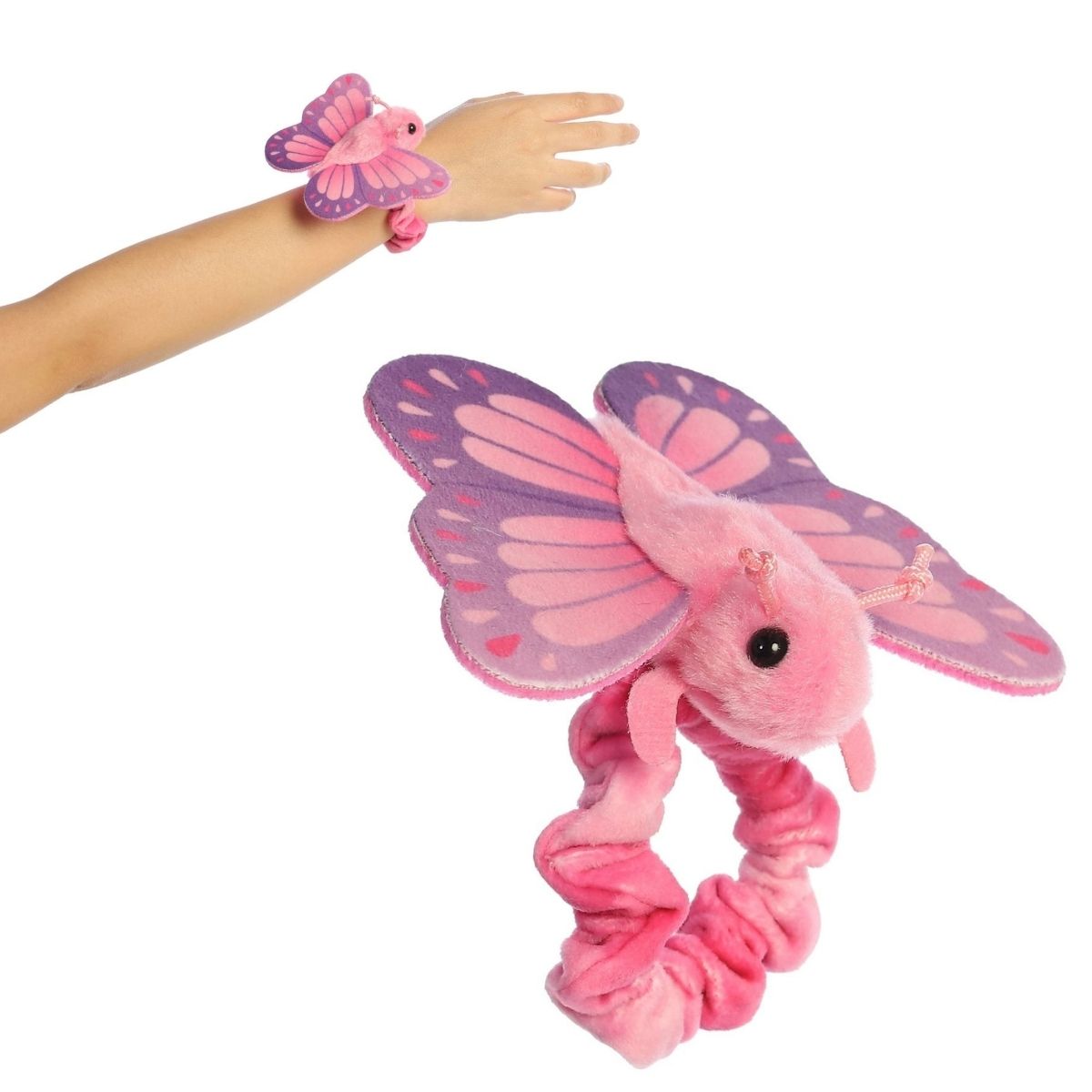 A person's arm wearing the 5-inch Aurora Wrist Flingers Blush Butterfly plush with a close-up of the pink butterfly attached to its wristband.