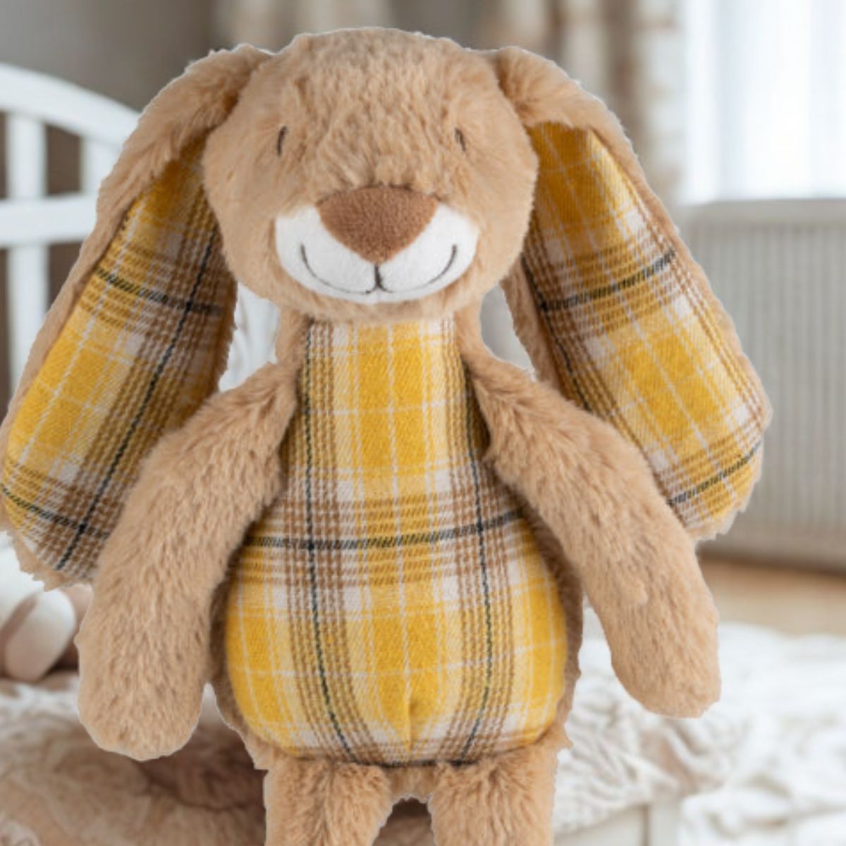 Close-up of the Happy Horse Rabbit Riley plush toy sitting on a cozy bed in a bright nursery.