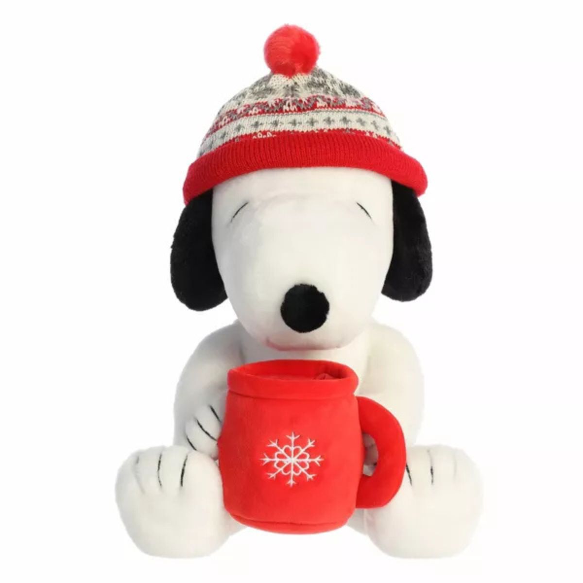 Aurora 12-inch Peanuts Winter Hat Snoopy plush toy sitting forward while holding a red plush mug with a white snowflake, wearing a red and grey patterned knit beanie with a red pom-pom.