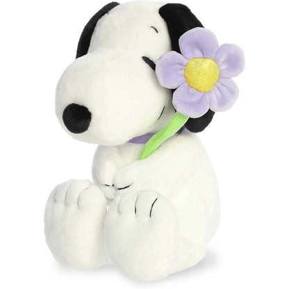 Angled front view of the 9-inch Aurora Peanuts Snoopy stuffed animal sitting down holding a purple flower.