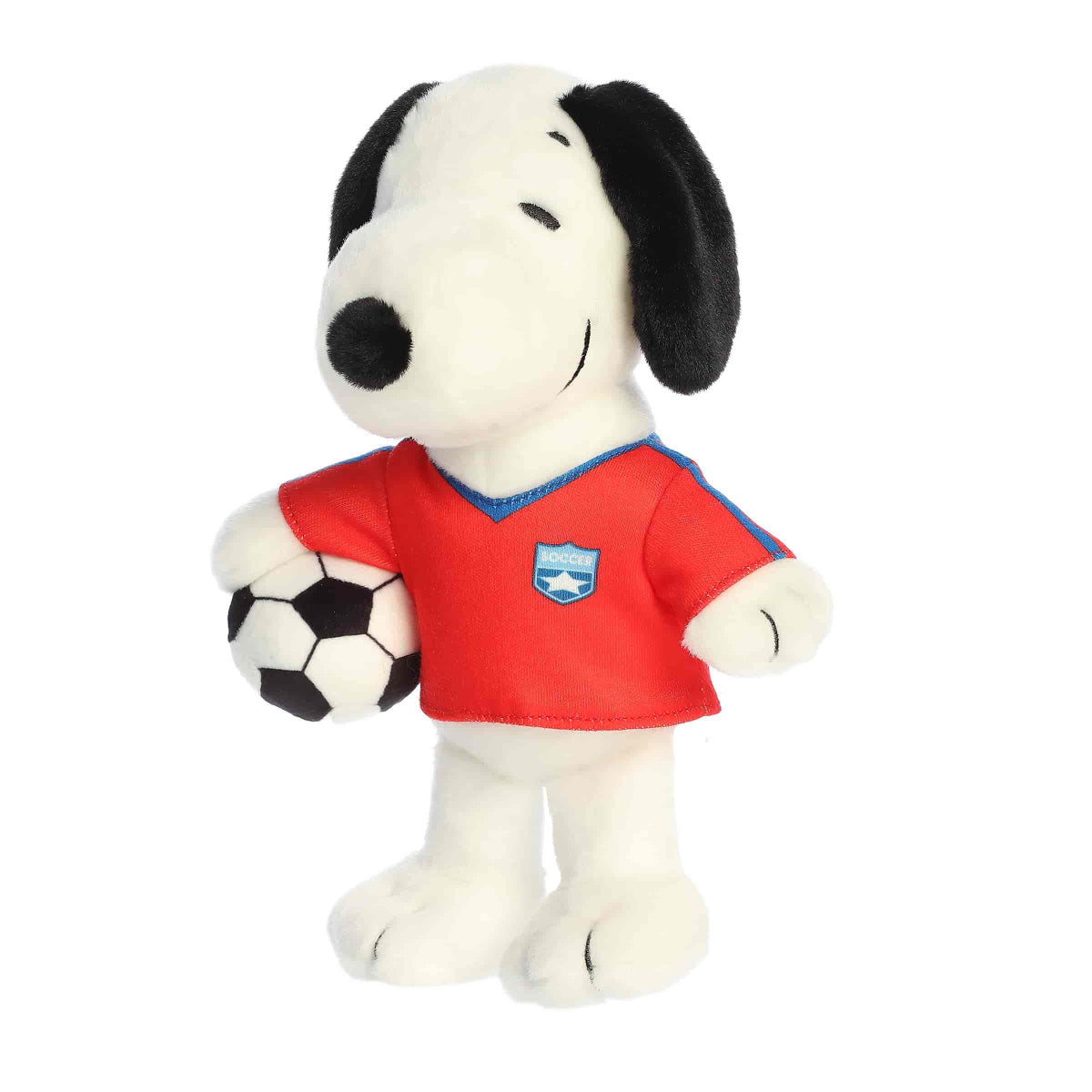 Angled front view of the Snoopy soccer plush toy standing on its feet while holding the soccer ball in its red jersey.