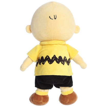 Back view of the Charlie Brown stuffed animal standing up, highlighting his black shorts and yellow shirt.