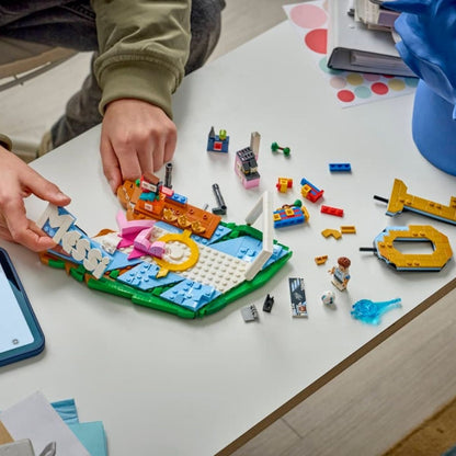 A pair of hands building the 500-piece LEGO® Lionel Messi soccer highlights set with scattered pieces on a table.