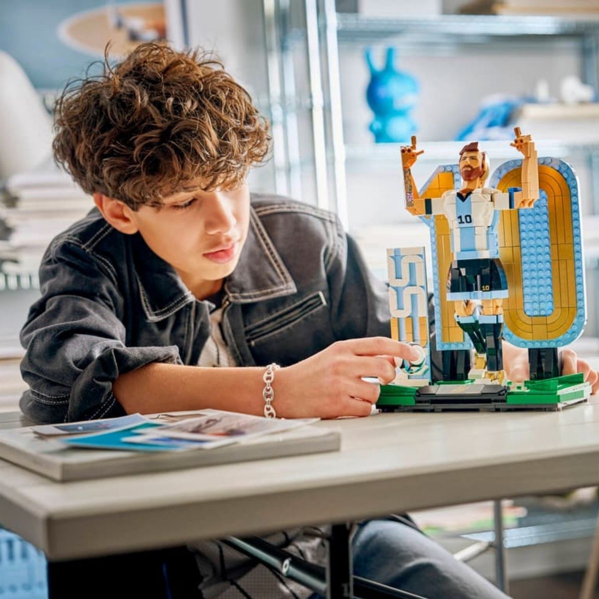 A teenage boy sitting at a desk assembling the 958-piece LEGO® Lionel Messi sports legend building set.
