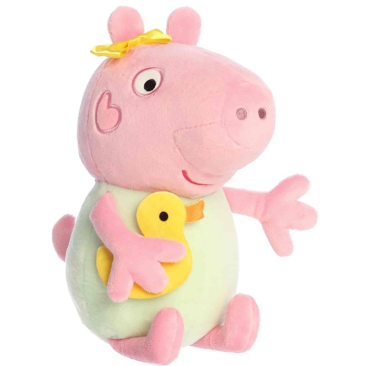 Aurora 12-inch Baby Evie pig plush toy sitting at an angle, featuring a pink body, a mint-green outfit, a yellow head bow, and holding a small yellow plush duck under her arm.
