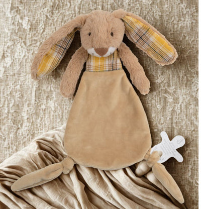 The Rabbit Riley plush lovey tucked into a soft, folded beige blanket on a textured neutral surface.