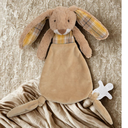 The Rabbit Riley plush lovey tucked into a soft, folded beige blanket on a textured neutral surface.