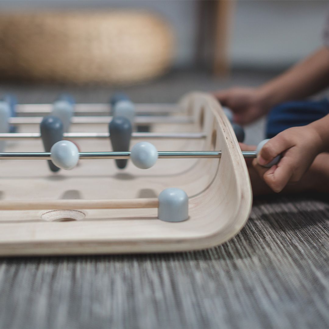 Close-up of a child's hands gripping the control rods on the durable PlanToys wooden soccer game.