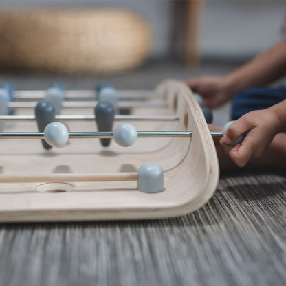 Close-up of a child's hands gripping the control rods on the durable PlanToys wooden soccer game.
