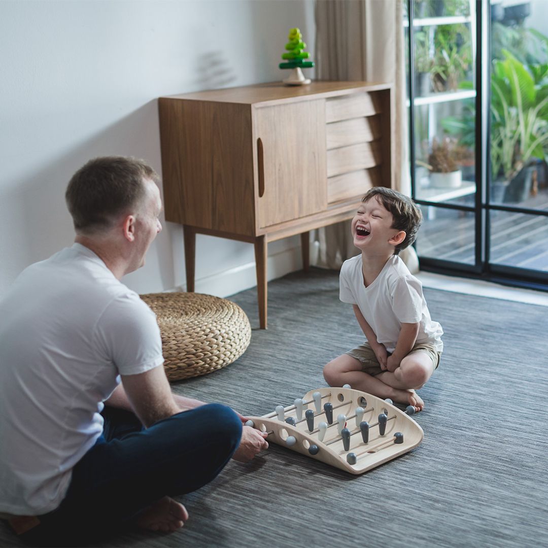 A father and son laughing and celebrating a goal during a fun family game of PlanToys wooden tabletop soccer.