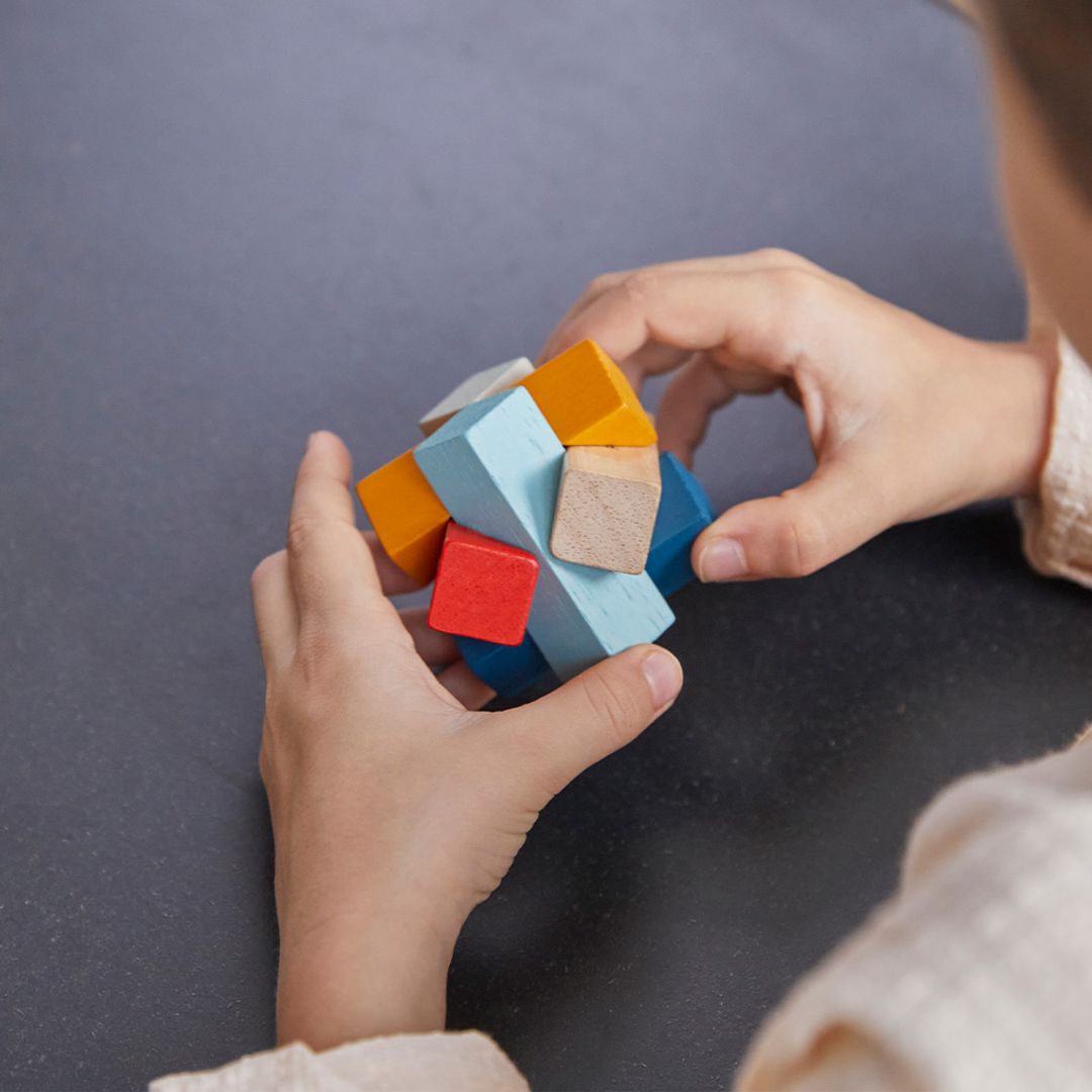 Detailed lifestyle shot showing a child's hands placing a colorful geometric block into the PlanMini puzzle frame.