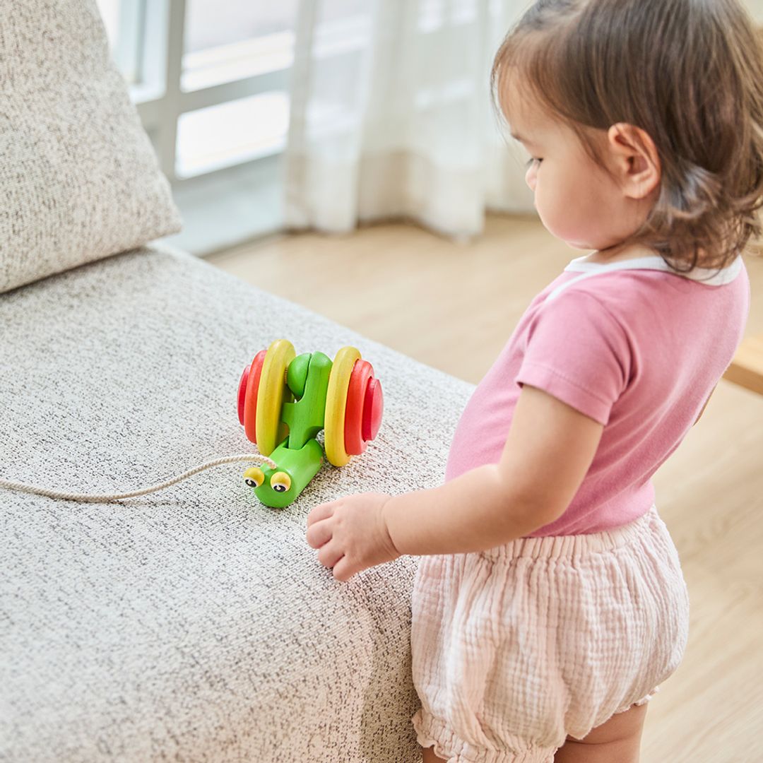 Child playing with PlanToys wooden pull-along snail toy on the chair.