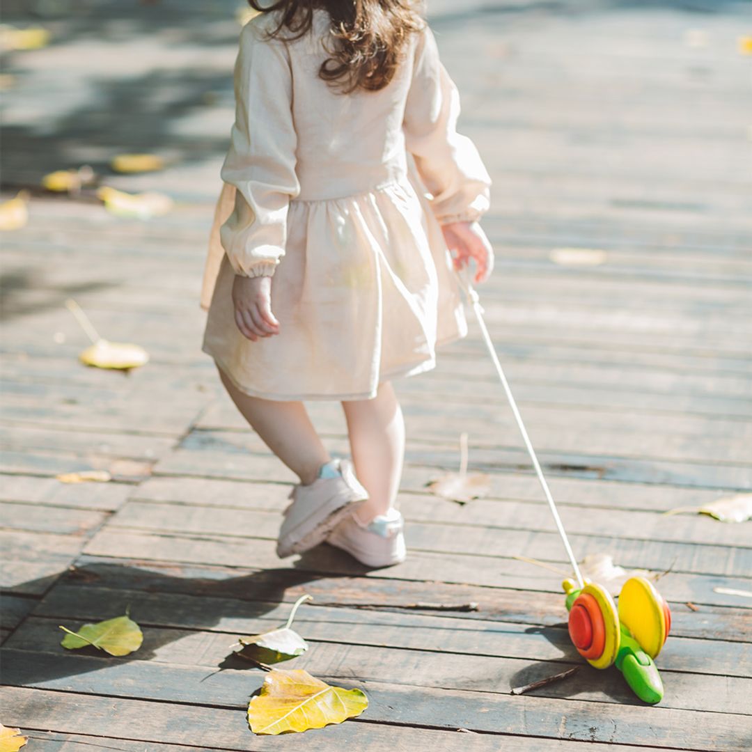 A happy child walking and pulling the PlanToys wooden pull-along snail toy across the floor.