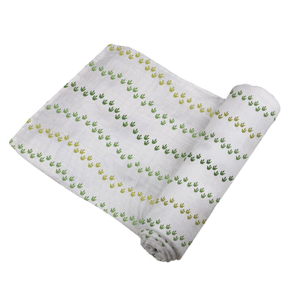 Angled view of the swaddle blanket partially unrolled to showcase the wavy lines of green dinosaur footprints.